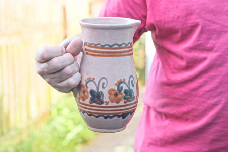 one man in red clothes holds brown old ceramic jug in hand on summer streetの写真素材