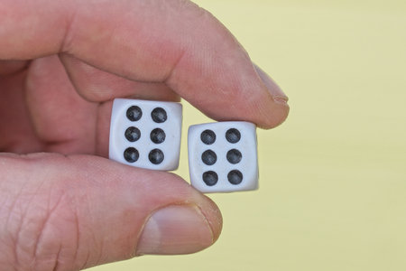 fingers of a hand holding two white dice on a yellow background