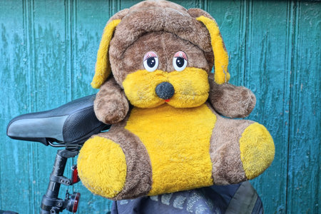 one big plush brown yellow toy dog sits on bike rack near green wall on summer street