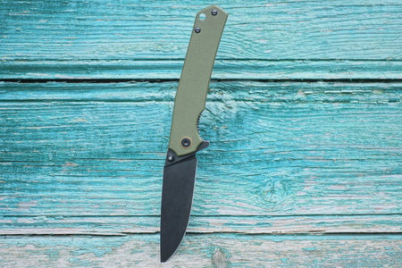 one folding knife with a black blade and a green handle sticks out of a wooden wall on the streetの写真素材