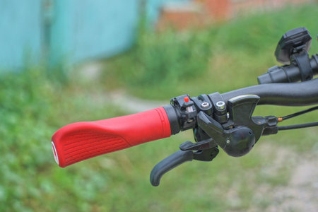 part of a black metal bicycle handlebar with a handbrake and a red plastic handle on a background of green grass in natureの写真素材