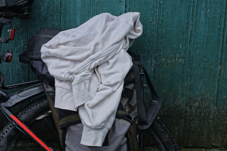 A single wrinkled white hoodie jacket lies on a bicycle rack near a green wall on a summer street