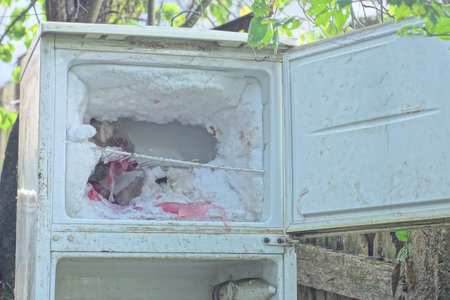 part of one old refrigerator with an open freezer compartment with white snow and ice inside on a summer streetの写真素材