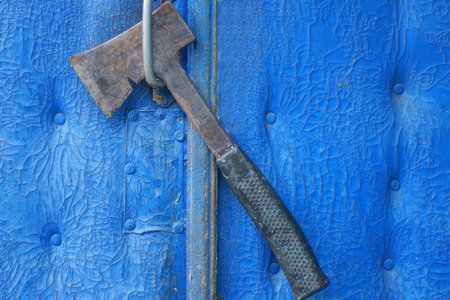 one old black gray ax hanging on a door handle on a blue wall outsideの写真素材