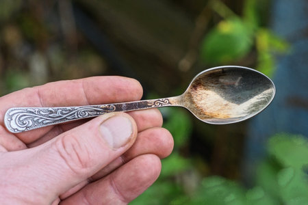 hand holding one small gray old metal teaspoon on summer streetの写真素材