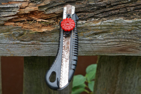 one black red plastic stationery knife with gray steel blade sticking out of an old wooden board