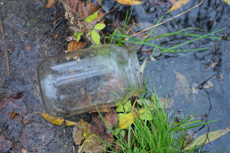 One dirty empty glass jar lies on the gray ground on the shore of a lake near the water on a summer...