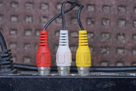 three colored old plugs with wires are connected to an electrical metal appliance on a brown...