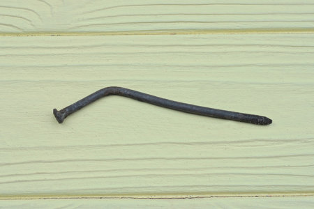 one old bent rusty iron nail lies on a yellow wooden tableの写真素材