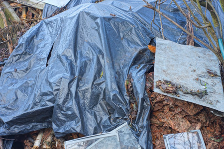 one big pile of brown firewood bark and branches covered with black plastic on a rural street