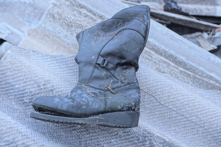 one old dirty black tarpaulin leather boot stands on the gray floor on the autumn street