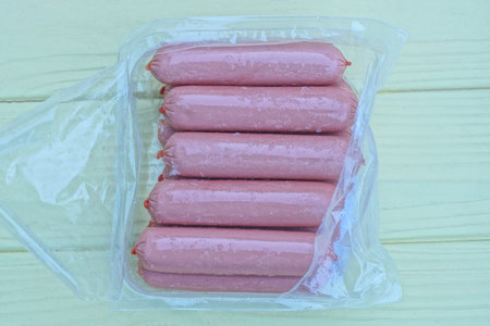 raw sausages in a torn transparent cellophane package lie on a yellow tableの写真素材