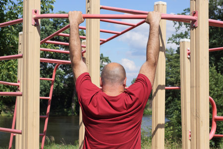 one male athlete in a red shirt pulls himself up on a sports horizontal bar on the street on a...