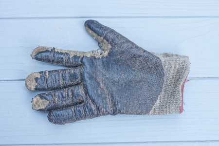 one rubber black gray dirty work glove lies on gray wooden table