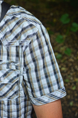 one hand of a man with a color rolled up sleeve of a shir twith a black backpack strap on his...