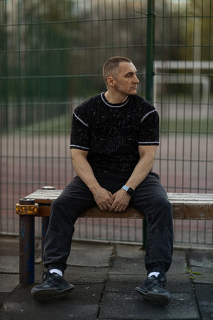 man sits calmly on bench gazing thoughtfully into distance. late afternoon light casts warm glow...