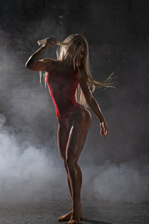 skilled blonde woman athlete stands confidently, highlighting her physique and graceful movement in red outfit, surrounded mist in dramatic settingの写真素材