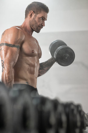 fit man with defined muscles is focused on his bicep curls while holding a dumbbell. This workout...