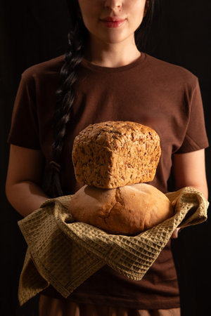 brunette girl in a brown T shirt holds a loaf of bread in her hands displaying it with care. The warm atmosphere suggests a homey baking experience in the kitchen.の写真素材