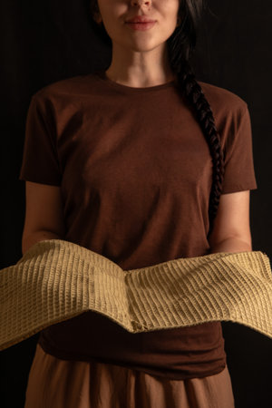 brunette girl stands with a warm smile holding fresh bread in her hands. She is dressed in a simple brown T shirt creating a cozy atmosphere.の写真素材