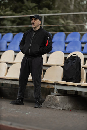 man dressed in a black bomber jacket and cap stands alone in the empty stands showing his emotions...
