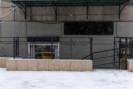 Snow falls heavily around the entrance of a basement store. The steps are slippery and the ground is blanketed in white indicating a winter storms intensity.の写真素材