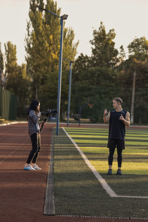 A woman records a video featuring an athlete on a sunny outdoor track. They are engaged in conversation while the sun sets creating a warm atmosphere.の写真素材