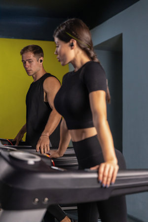 sporty girl runs on a treadmill while a man walks beside her. Both are focused and wearing...