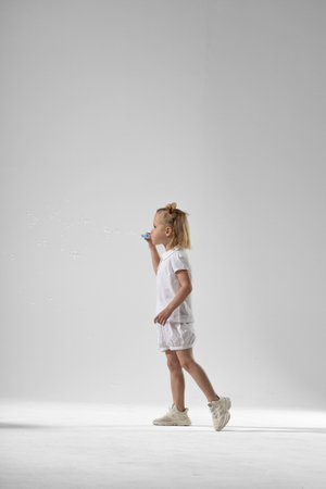 little blonde girl joyfully blows soap bubbles her face filled with delight as she watches them float and pop enjoying a playful moment.の写真素材