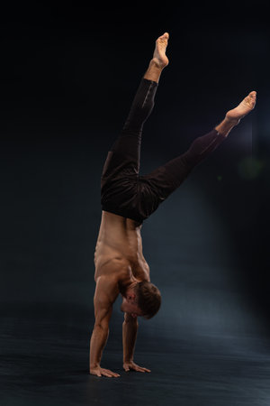 skilled athlete balances on one hand showcasing strength and control. The setting is a dimly lit studio with a soft spotlight highlighting his form during the impressive pose.の写真素材