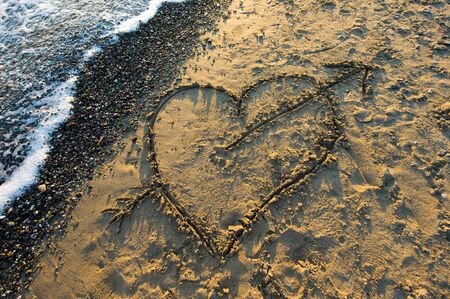 A heart with an arrow drawn in sand on a beachの写真素材