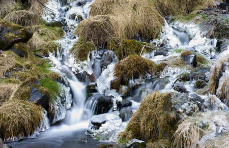 A small waterfall mainly frozen floating through the grass in the winterの写真素材