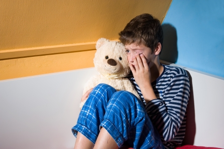A young boy is crying on his bed in his bedroomの写真素材