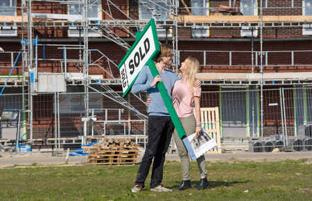 Young couple with blueprint is happy in front of their new built house they just bought