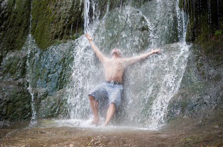 A man is having a shower underneath a natural waterfallの写真素材