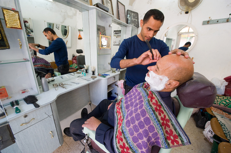 HEBRON, ISRAEL - 10 OCT, 2014: A barber is shaving a man in his small barbershop in the center of the old city of Hebronのeditorial素材