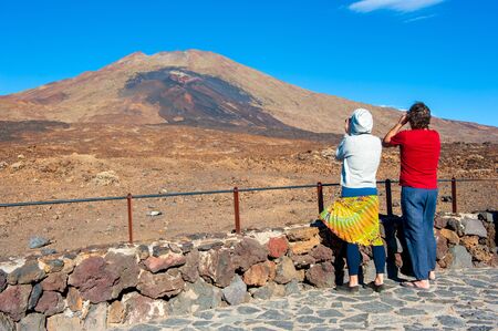 CANARY ISLAND TENERIFE, SPAIN - DEC 24, 2019: Tourists with binoculars watching the purple and brown lava from the lower vents of the volcano Pico Viejo on Canary Island Tenerife.のeditorial素材