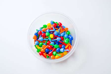 Small multi-colored plastic parts of children's mosaic in a transparent round container on a white background.の写真素材