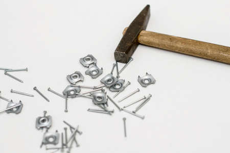 Small nails, furniture fittings and an old hammer with a wooden handle on a white background.