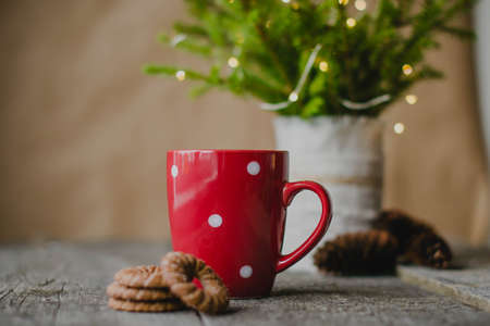 Red Cup with white polka dots on old wooden table (background). In the background, a Christmas tree with lights garlands.の写真素材