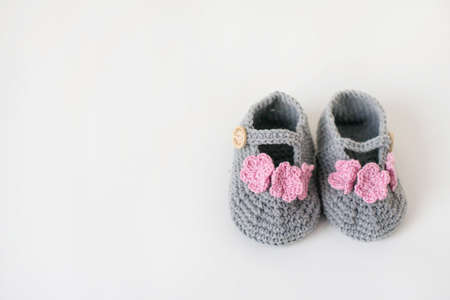 Gray booties shoes crocheted. Gray booties for girls with pink flowers and a wooden button on a white background. Copy space.の写真素材