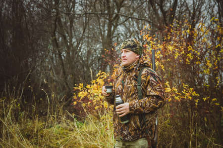 Hunter at a halt, drinking tea . A man in camouflage clothing with  a gun in a case.
