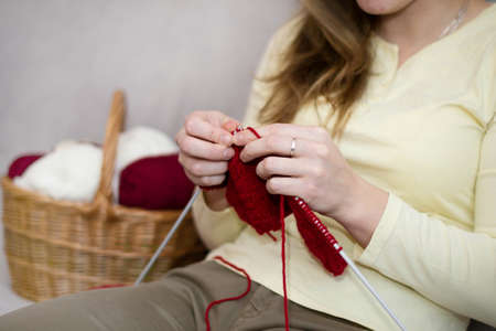 A woman knits on a knitting needlework made of red yarn. Knitting needles in the hands of a woman.