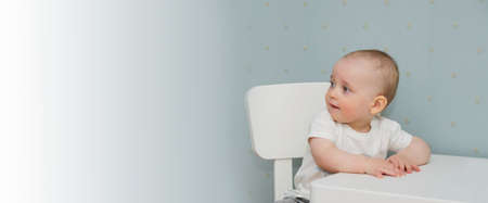 The kid sits on a chair at the table and looks away. Copy space bannerの写真素材