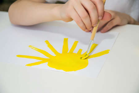 A child paints a yellow sun at a white table.の写真素材
