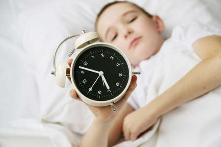 cute little boy hand turned off alarm clock on bed in sunlit, sleep and relaxation concept.の写真素材