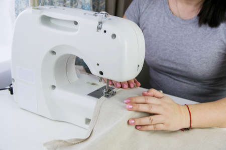 Modern sewing machine on a white table. A woman sews from linen fabric on a sewing machine.