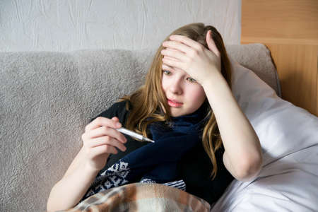 The girl is sick and lies in bed, measures the temperature and is surprised at the high temperature.の写真素材