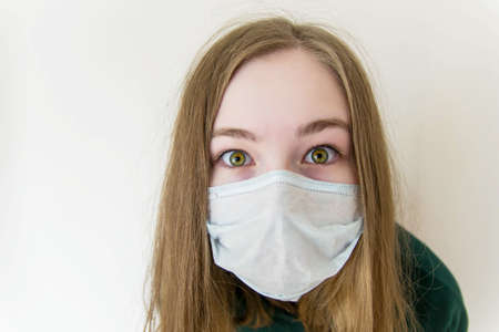 Girl in a medical mask closeup surprised, bulging, scared eyes.の写真素材