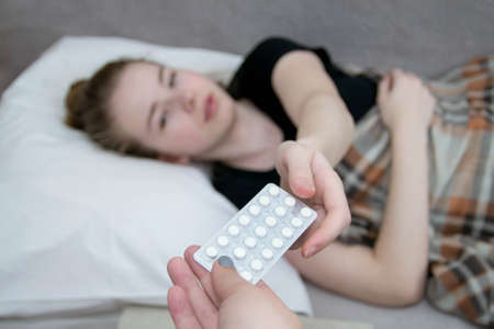 The girl lies in bed, is sick and takes pills from her hands for treatment. Pain during menstruation in a teenage girl.の写真素材